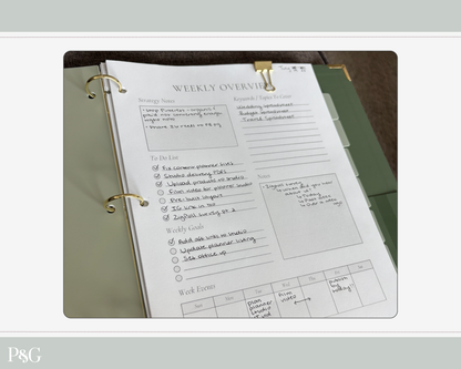 A weekly overview planner insert page from a three-ring binder, shown open on a dark surface. The page includes labeled sections for strategy notes, to-do list, notes, weekly goals, and work events, with handwritten entries.